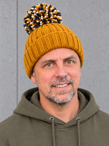 ESSENTIALS Sherpa Bommel Beanie Mustard – Mütze getragen von Olli, Kopf-Schulter-Nahaufnahme #color_mustard